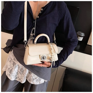 Vue détaillée du petit sac en cuir verni crème avec fermoir rotatif et breloque tressée