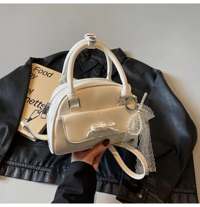 Detail view of cream mini bowling bag with bow decoration and pearl lace charm accessory