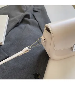 Detail of silver rectangular metal lock and stitching on creamy white leather saddle bag