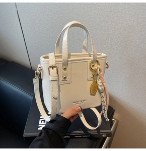 Detailed close-up of beige crossbody bucket bag with gold hardware and tennis charm