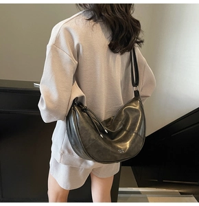 Détail d'un sac demi-lune noir en cuir souple porté à l'épaule par un mannequin