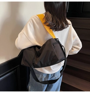 Détail du sac Boston en toile noire avec bandoulière jaune et gaufrage de marque