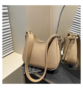 Gros plan sur le cuir beige grainé de litchi et boucle dorée d'un sac hobo élégant