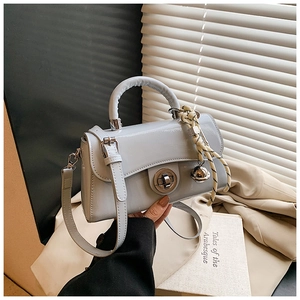 Détail du sac à main bleu-gris en cuir verni avec fermoir argenté et breloque tressée