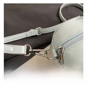 Detailed close-up of high-shine silver metal hooks and zipper on light blue patent leather bag