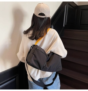 Détail du grand sac messager en toile noire avec bandoulière jaune sur le mannequin