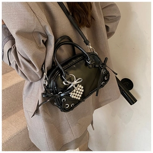 Gros plan détaillé d'un sac Boston en cuir verni noir avec un nœud et un charm cœur argenté