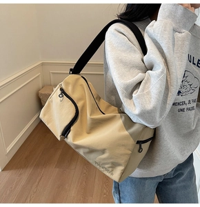 Vue latérale du sac bandoulière en toile beige avec bandoulière noire porté par modèle