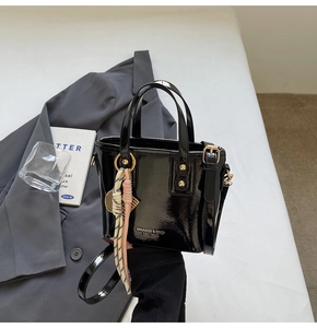 Detail of a black patent leather bucket bag with silk scarf and logo print