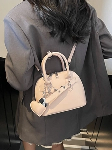 Beige shell-shaped crossbody bag with heart charm and silver chain on model