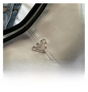 Macro shot of silver leather texture and signature triangular metal logo on tote bag