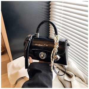 Détail du sac à main en cuir verni noir brillant avec fermoir rotatif et breloque tissée