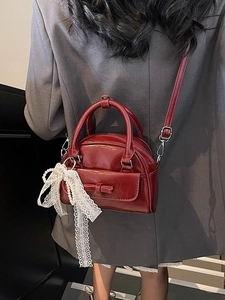 Glossy deep red mini bowling bag with bow and pearl lace charm on grey suit