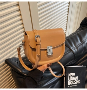 Detail of caramel saddle bag showing the metallic square buckle and smooth leather texture