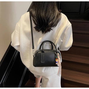 Detail of black litchi texture boston bag with colorful beaded charm on white hoodie
