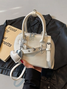 Elegant cream shell handbag with heart charm and silver hardware shown in a stylish setting