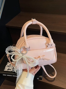 Pale pink glossy bowling bag with decorative bow and pearl lace charm on a wooden background