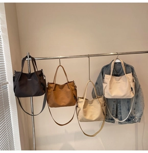 Borse tote in tela color caffè, caramello e beige appese su un supporto con tracolla