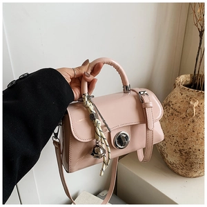 Détail d'un sac bandoulière en cuir verni rose clair avec fermoir rotatif et sangle tressée