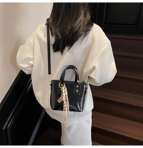 Detail of a black glossy mini bucket bag with decorative charm worn with a white hoodie