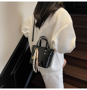 Detail of a black patent leather bucket bag with metallic studs and silk scarf accessory