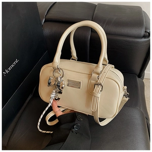 Detail view of beige Boston bag with ribbon charm and logo plate on leather surface