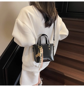 Detail of a black glossy bucket bag with woven tassels on a dark wood staircase