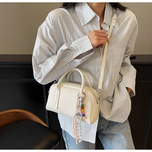 Detail of white lychee leather handbag with colorful beaded charms and crossbody strap