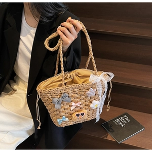 Détail du sac seau en paille tressé avec breloques décoratives et doublure à cordon serrage