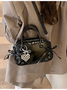 Sac Boston noir brillant avec nœuds et breloque cœur porté par un mannequin chic
