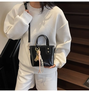 Close-up of black patent leather mini bucket bag with gold hardware and woven charms