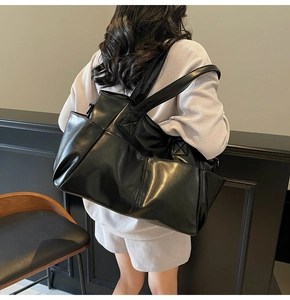 Close-up of black glossy leather tote bag showing reinforced stitching and front pocket