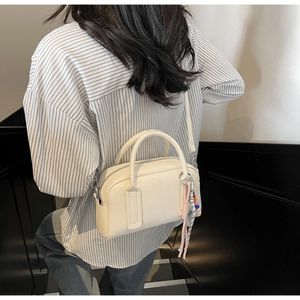Detail view of cream textured leather crossbody bag with beaded charm on shoulder