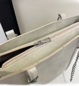 Detail of silver smooth metal zipper and embossed lettering on off-white tote bag