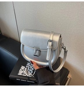 Close-up of metallic silver saddle bag featuring a rectangular metal buckle and adjustable strap