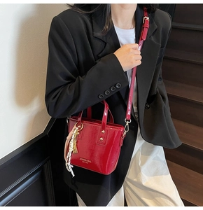 Detail of red patent leather bucket bag with logo and decorative silk scarf on model
