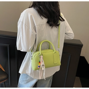 Detail of light green pebbled leather handbag with beaded charm and silk ribbon on model