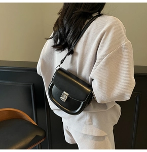 Detail of a black matte leather saddle bag with silver metal clasp on a model