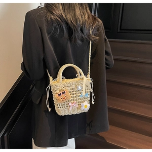 Detail of beige woven straw bucket bag featuring cute bear and floral charms on strap