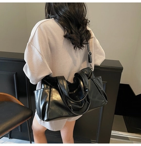 Rear view of model holding a black faux leather tote bag with dual handles and side pocket