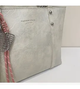 Detail of silver grey tote bag with metallic texture, embossed text and pink tennis charm