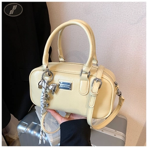 Detail view of cream Boston bag with silver logo plate and bow charm accessory