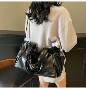Modern black glossy tote bag with adjustable strap shown on model in a minimalist setting