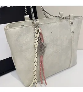 Close-up of light gray tote bag featuring a tennis racket charm and metal chain strap