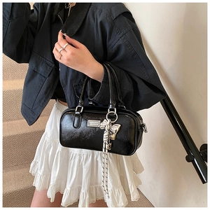 Close-up of black patent leather handbag with silver logo plate and tassel detail