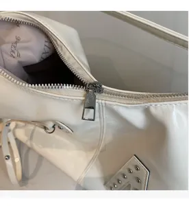 Close-up of smooth silver zipper and logo lining on white leather shoulder bag
