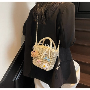 Detail of hand-woven straw bucket bag with floral charms and ribbon on model's shoulder