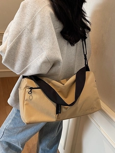 Grand sac Boston en toile beige avec bandoulière noire porté par un mannequin en ville