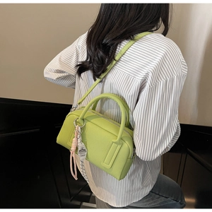Green leather crossbody bag with leaf charm shown on model in striped shirt