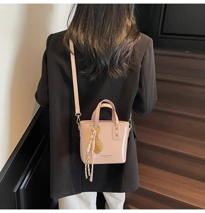 Pink patent leather bucket bag featuring a crossbody strap and brand text details